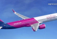 Side profile of a Wizz Air Airbus plane in flight against a bright blue sky with light clouds, showing the distinctive purple and pink livery and logo.
